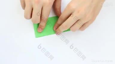 小伙子的手在白色背景上用绿色的纸做折纸鹤